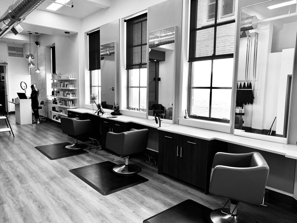 A black and white image of a salon with chairs and mirrors